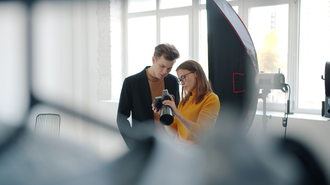 services-02 Girl and guy model are talking in photo studio watching pictures on digital camera standing indoors together communicating after photo shoot. Youth and technology concept.