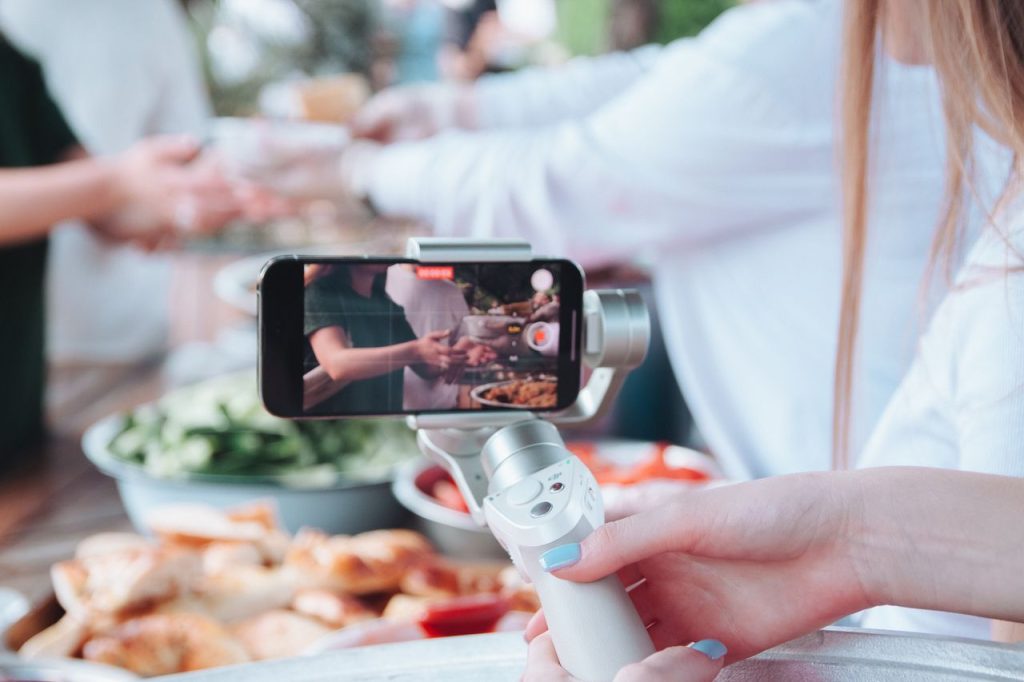 woman-hand-holding-tripod-and-recording-video-with-smartphone-17274195 A person uses a smartphone gimbal to film a food event with various dishes.