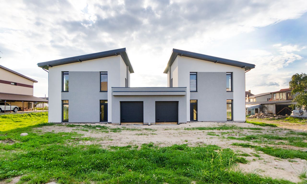 töitämme Front view of twin modern houses with a symmetrical architectural design under a cloudy sky.